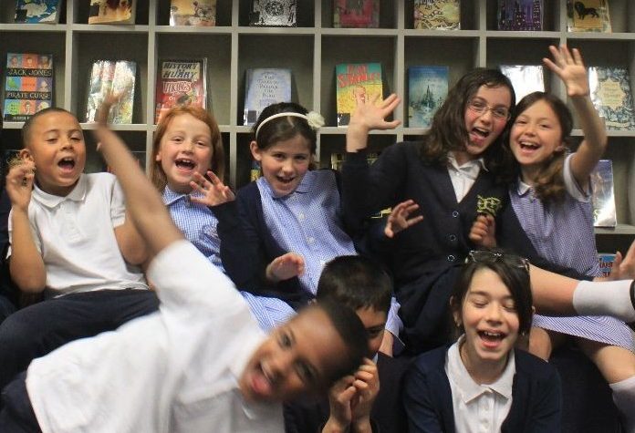 The now>press>play Children's Advisory Board. Eight children smile and sit in their school library.