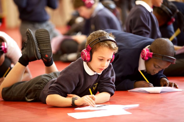 Group of children complete Now Press Play worksheets while wearing pink headphones