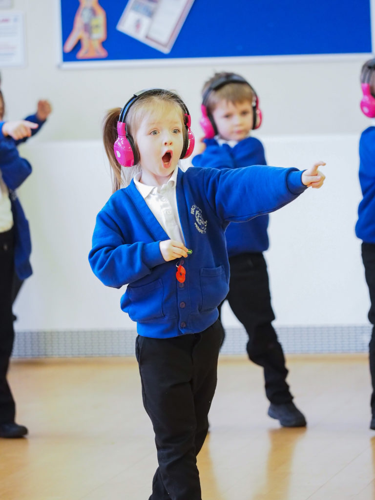 A student from Birchwood School points, shocked, off screen. She's wearing pink headphones and doing the Now Press Play Guy Fawkes Night Experience