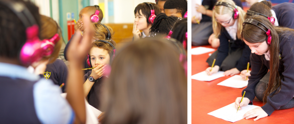 School children revise for their SATs using Now Press Play. They're wearing a blue school uniform and pink headphones, and writing on worksheets as they listen.