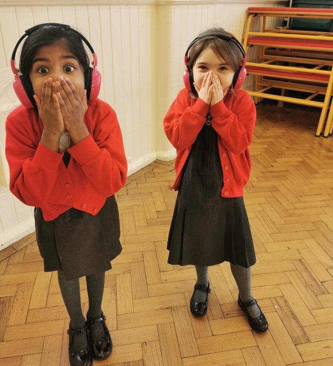 Two Cheam Commons infants students look shocked as they listen to Now Press Play through their pink headphones.