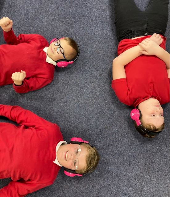 Three Chiltern students enjoy listening to Now Press Play while they lie on the floor of a classroom.