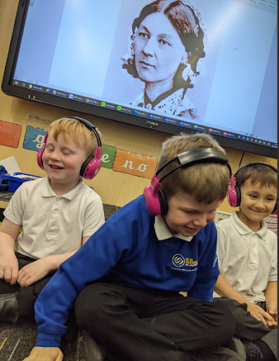 Three school students listen to Now Press Play in a classroom. On the interactive whiteboard behind them is a picture of Florence Nightingale.