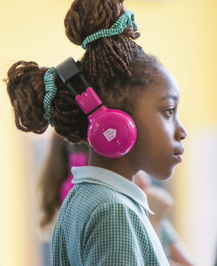 A young girl wears pink headphones, looking to the right