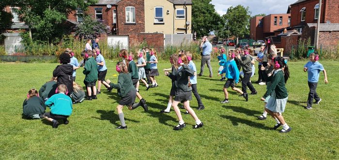 A group of children running in their school field while using Now Press Play