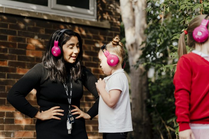 A teacher and child wearing pink headphones using Now Press Play