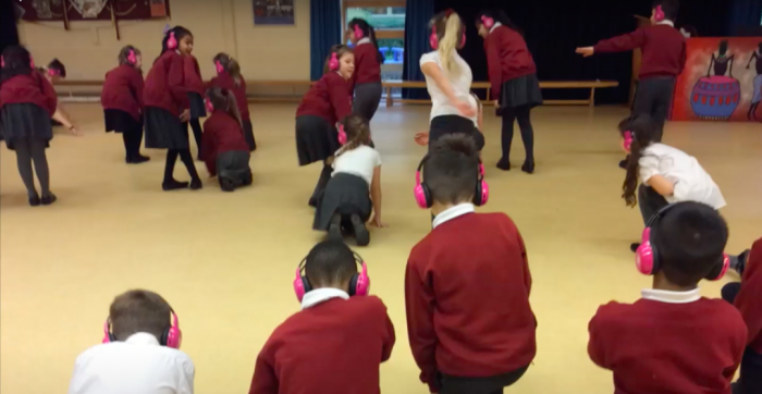 Children at Woodland View Primary School kneel while using Now Press Play in their school hall.