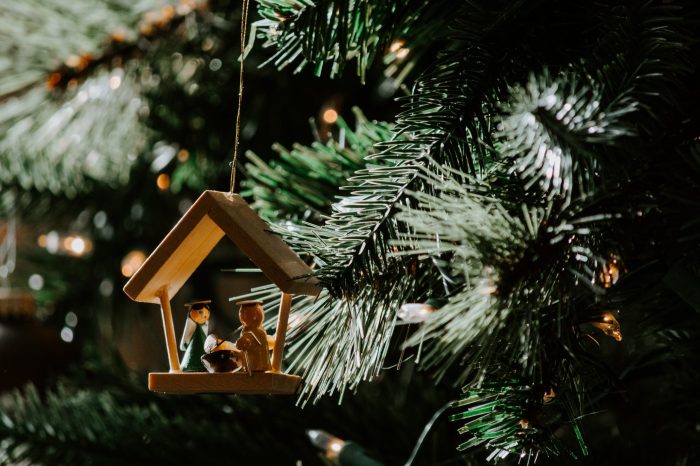 A small wooden carving of the nativity scene is hung from a Christmas tree.