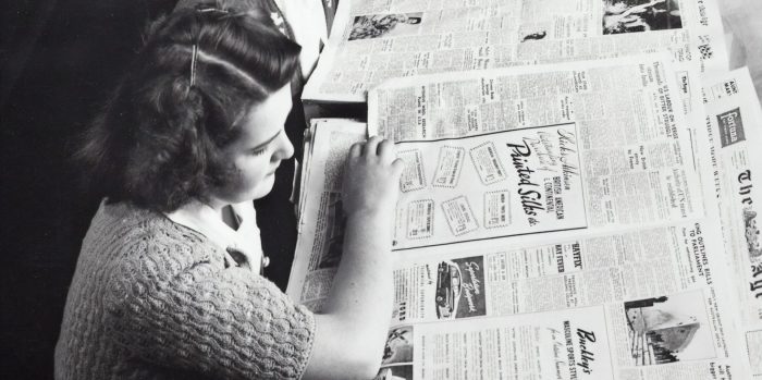 Two women sit in a row reading newspapers.