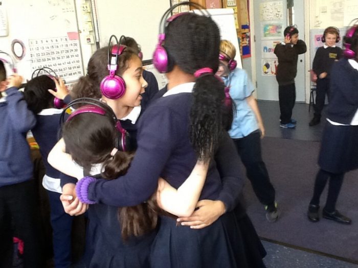 A group of KS2 school children hugging and interacting in a classroom while using Now Press Play as part of their curriculum.
