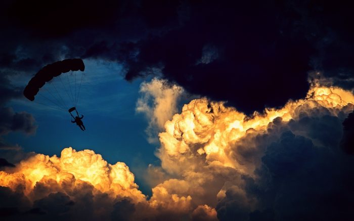 A person parachutes through a cloudy sky.