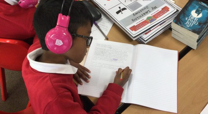 A boy listens to sound stimuli through Now Press Play headphones while in a writing lesson